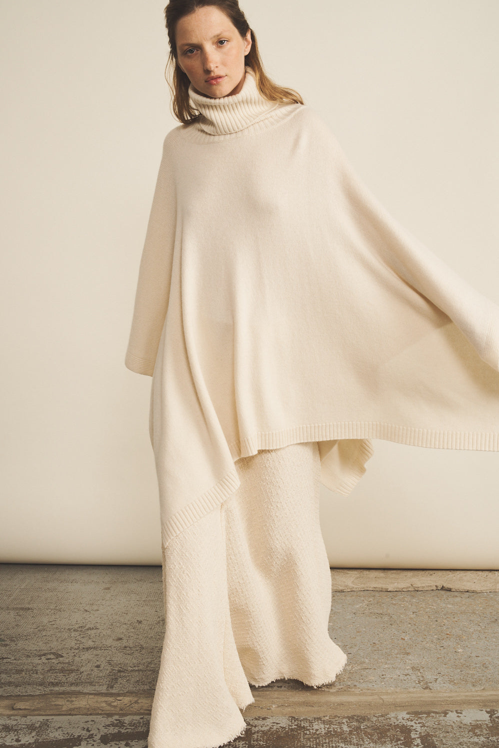 A woman look wearing an oversized white turtleneck cashmere poncho with cut-sides, paired with white pant | Angela | Linnea Lund